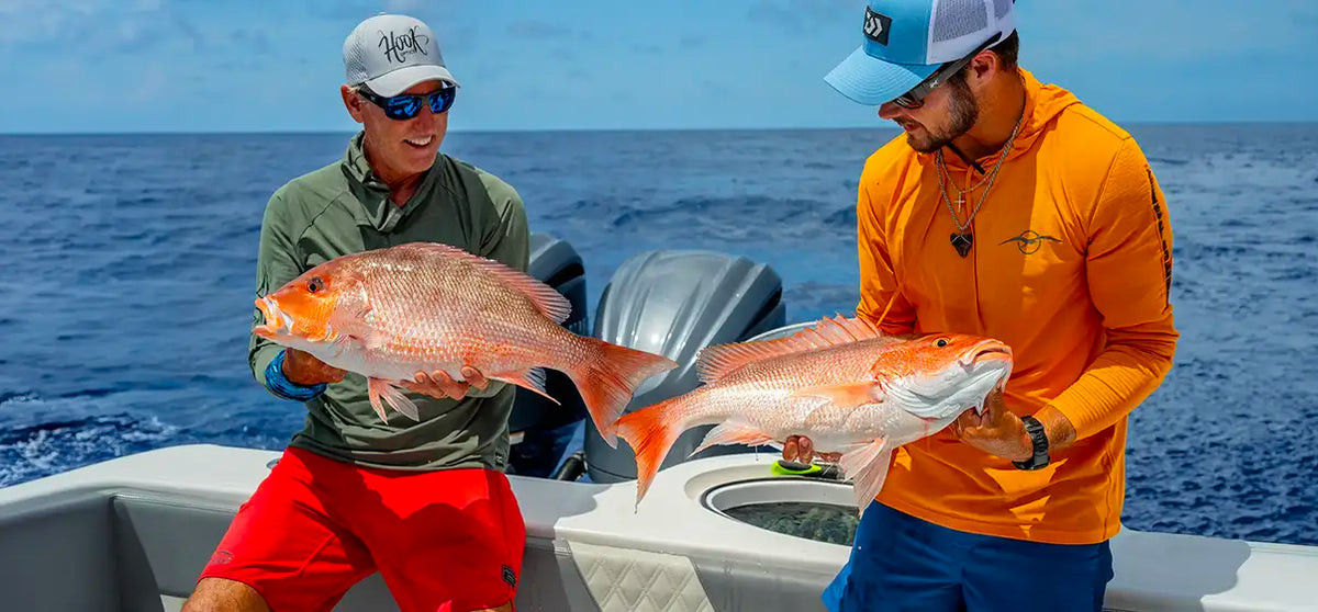 Captains from Into the Blue wearing Hook Optics Sunglasses on a boat holding large red fish, wearing outdoor fishing apparel including a green shirt, red shorts, and an orange long-sleeve top against the ocean background.