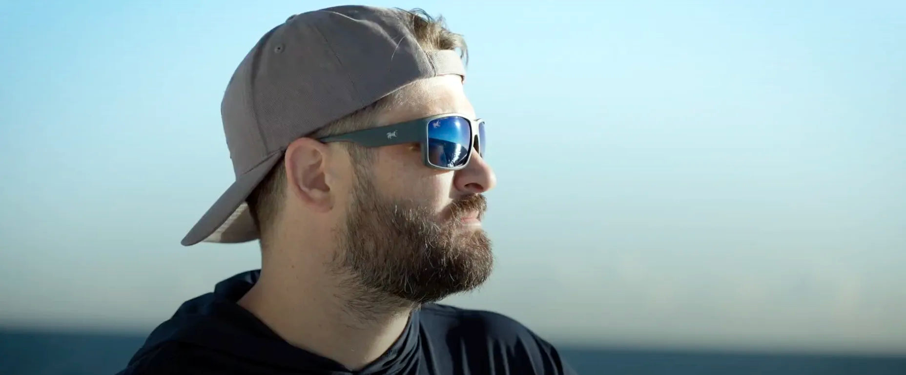 Man wearing hook sunglasses and a cap with a clear sky background