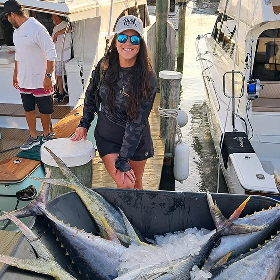 Woman standing next to a boat with a large catch of fish on ice at a dock she caught wearing hook optics