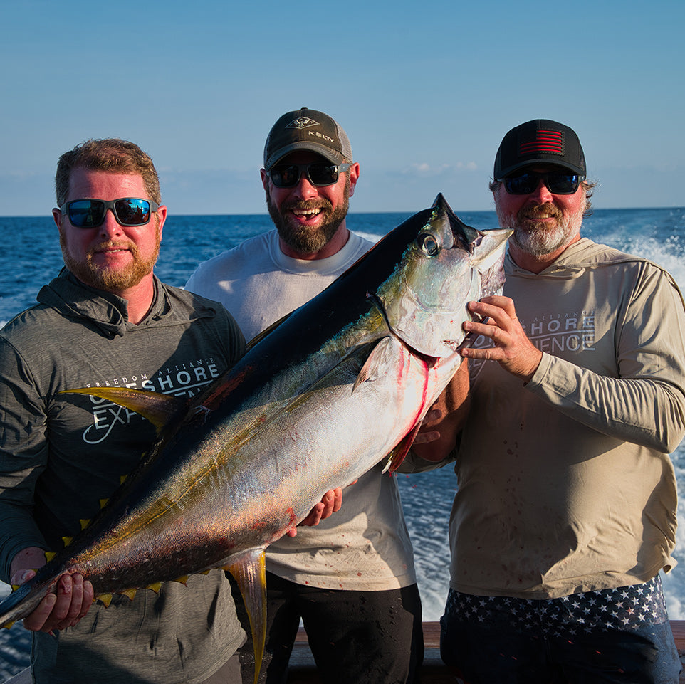 Three men on a boat holding a large fish with ocean in the background wearing hook optics sunglasses